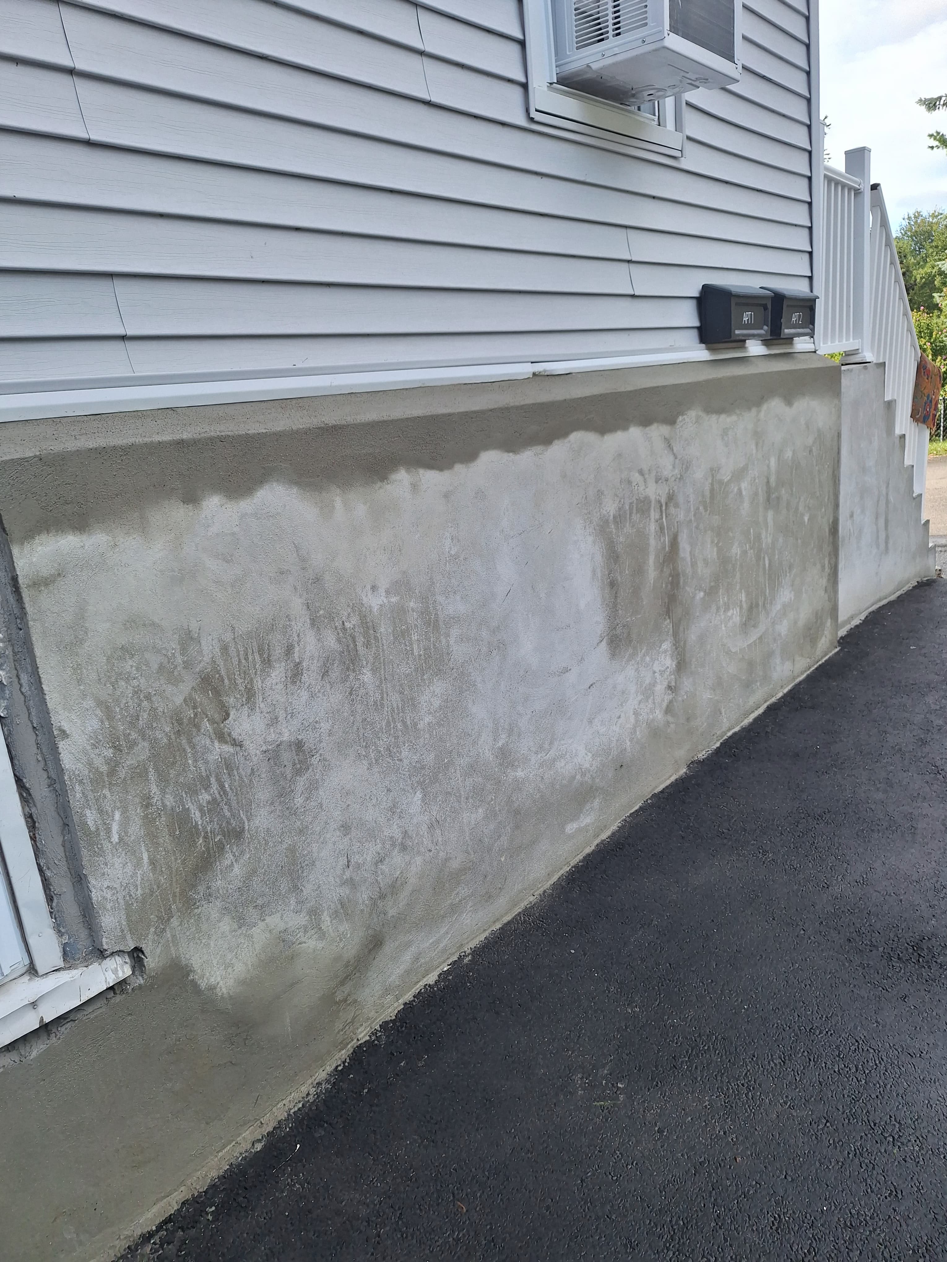 Concrete foundation wall with water stains and moisture marks near house