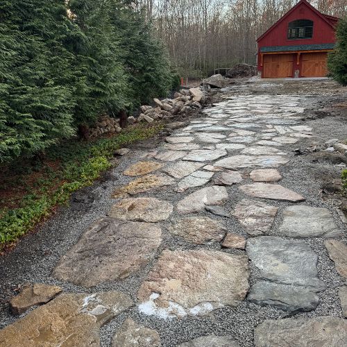 Stone pathway leading to red wooden barn surrounded by evergreen forest