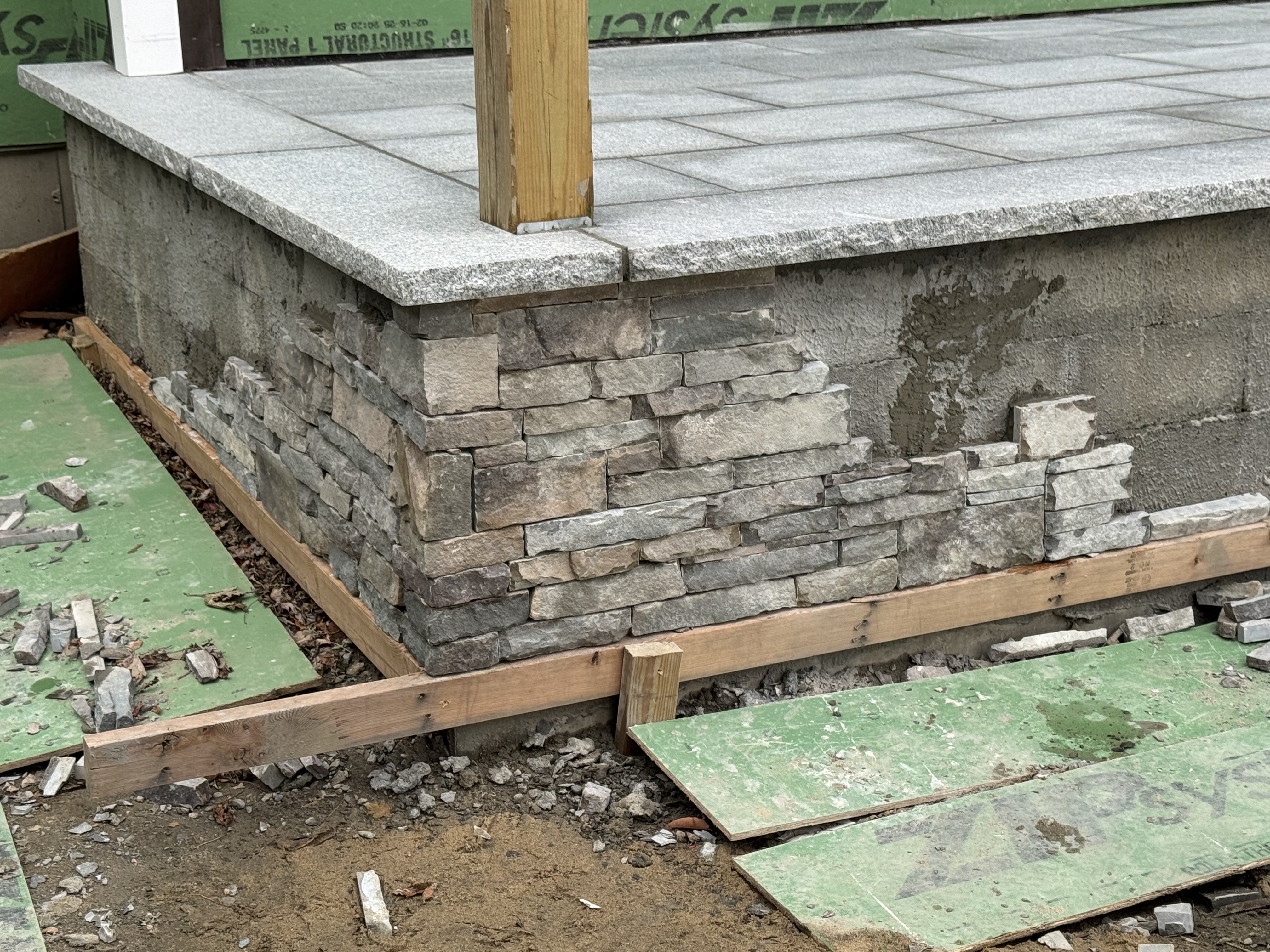 Stone veneer wall construction with wooden supports and granite cap
