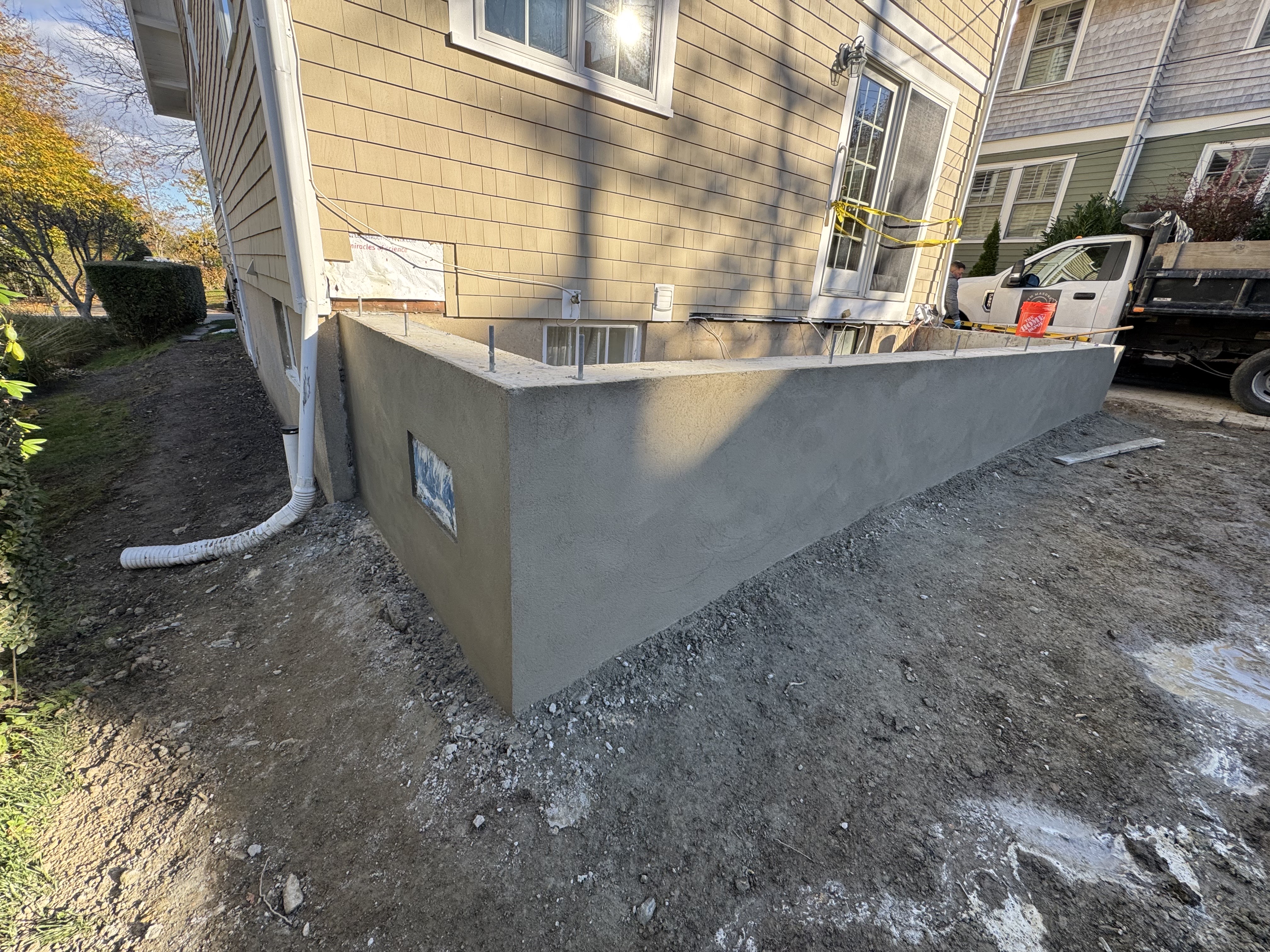Concrete foundation wall with window, attached to yellow house under construction
